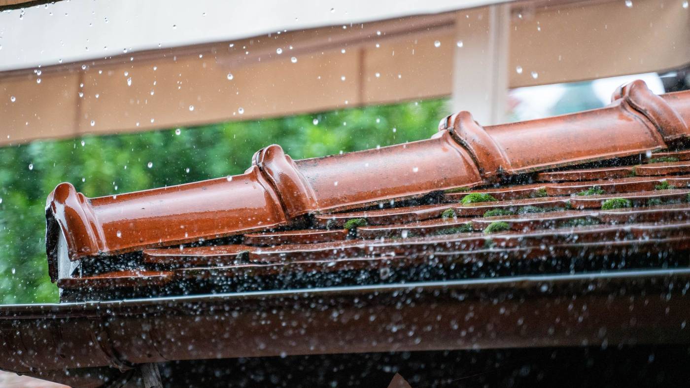 Eau de pluie s'écoulant d'une gouttière le long d'un toit en tuiles